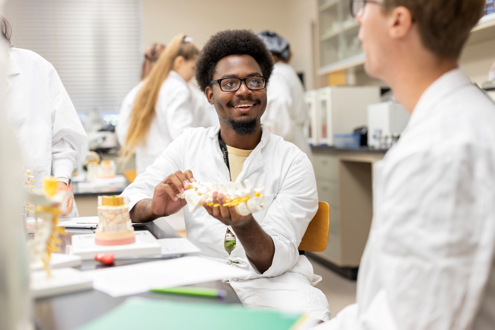 Two students discussing while one holds a model of the spine and vertebrae